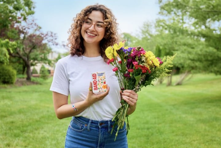 Woman smiling and holding a colorful flower bouquet and a box of BAND-AID wildflower bandages