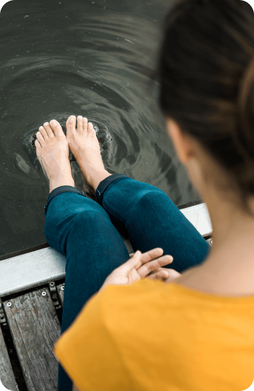 Woman looking at her feet while sitting on a dock and putting her toes in the water.
